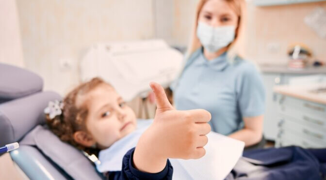Female dentist and cute little girl giving thumbs up.