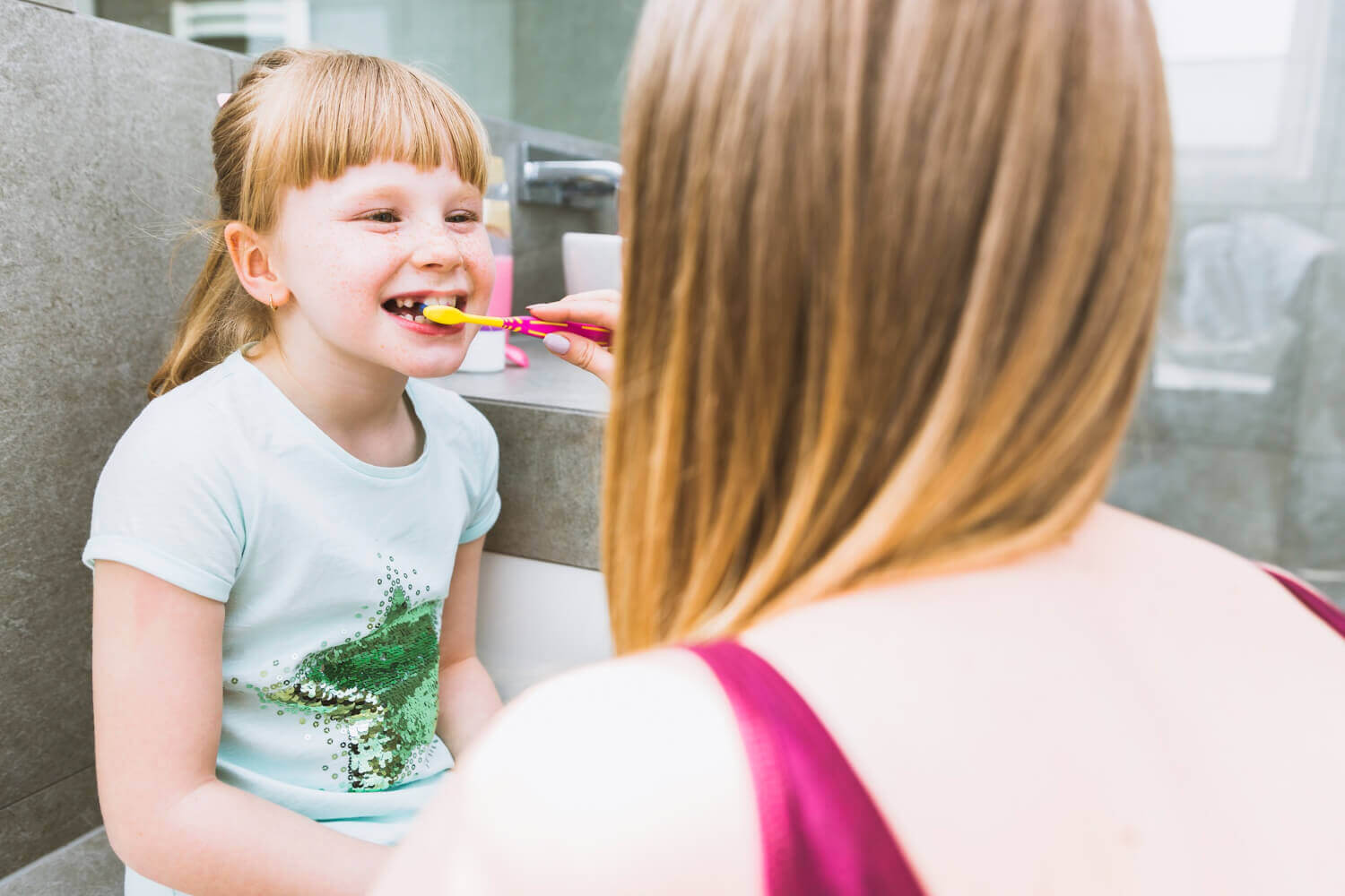 faceless mother brushing teeth daughter