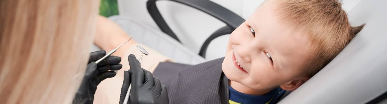 Cheerful little boy sitting in dental chair in dental office.