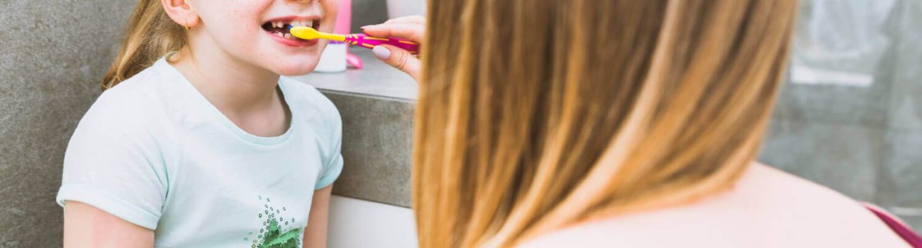 faceless mother brushing teeth daughter